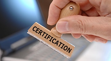 A hand holding a rubber stamp. The word Certification is on the side of the stamp.