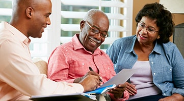 A financial adviser speaking to an elderly couple. They are looking at a document and smiling.