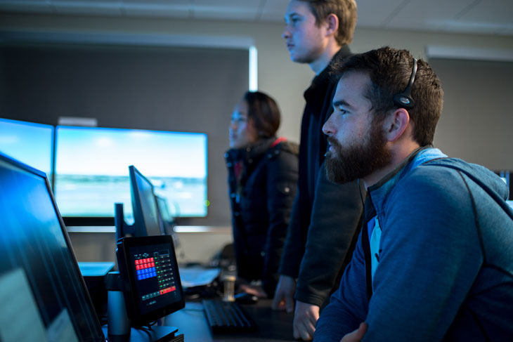 Three students looking on in aviation classroom