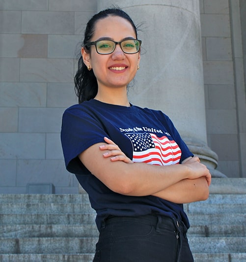 Nigina posing with her arms crossed in front of a stone building.