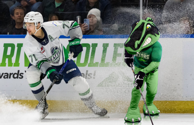 Green River College gator mascot skating on the ice with a Seattle Thunderbirds hockey player.