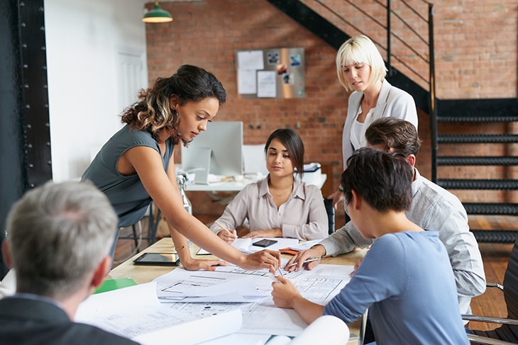 photo of a workplace team gathered around a table looking at project documents