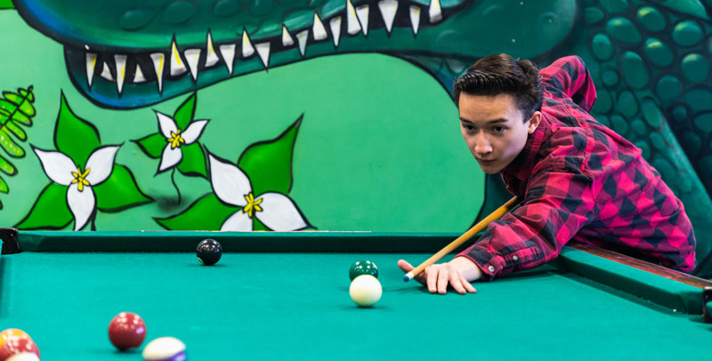 student plays pool in SU in front of Gator mural