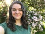 Picture of Victoria smiling in front of a backdrop of green trees